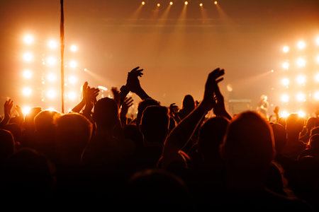 An enthusiastic audience applauds a performer during a live show. Bright orange stage lights create...