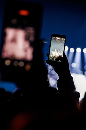 Point of view shot of an audience member recording a live music performance on a smartphone. Dark...