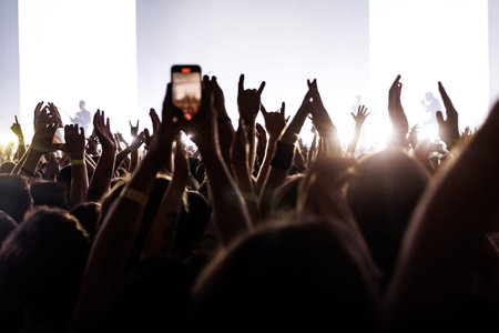 Audience members cheering and waving hands during a performance at a music venue with bright...