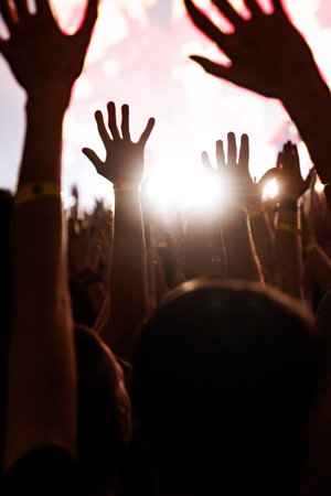 A low-angle shot of many hands reaching toward a bright, white light source on a concert stage,...