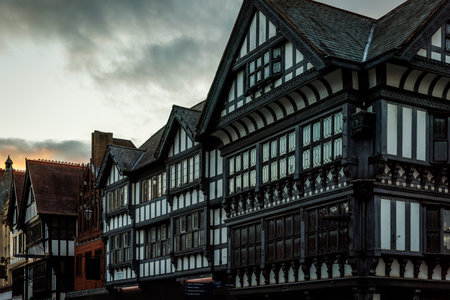 Traditional black and white timber framed architecture lines a historic street under a moody, cloudy...