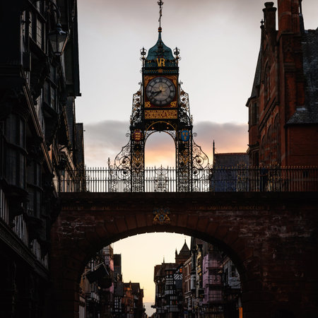 The ornate Victorian clock tower stands over a street between historic buildings under a colorful...