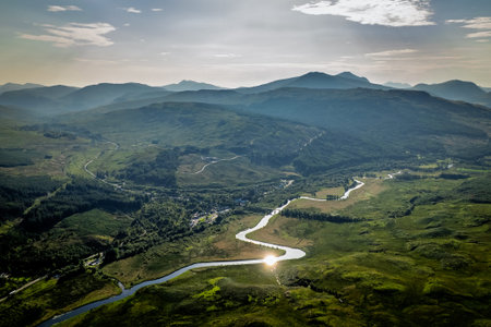 A high-angle drone perspective of a shimmering river snaking through green valleys and mountains...