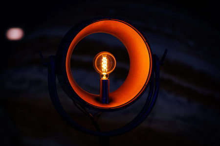 A minimalist light fixture featuring a round orange frame and a filament bulb at the center. The...