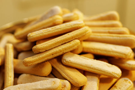 A macro shot of Italian savoiardi biscuits stacked together. The image highlights the sugary texture...