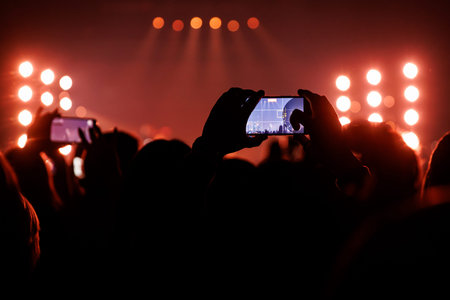 A silhouette of a person holding a phone horizontally to record a show with red lights.