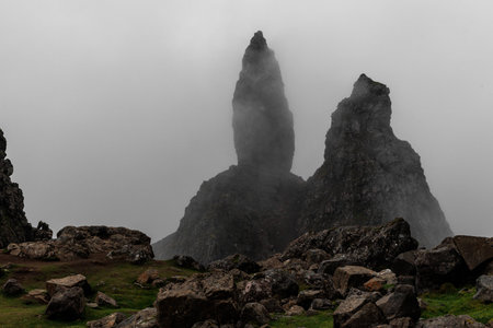 Dramatic black rock pinnacles rise from the earth, partially obscured by thick grey fog and clouds....