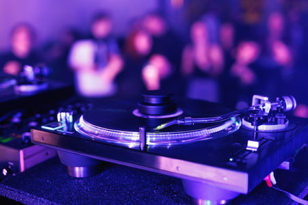 A close-up of a record player spinning a disc with purple and blue ambient lighting and a blurred...