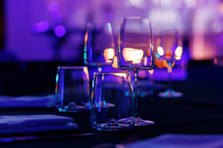 Empty professional glassware arranged on a dark table at a luxury event with colorful bokeh and neon lights.の写真素材