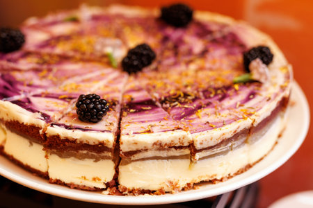 A close-up of a creamy multi-layer cheesecake topped with purple fruit swirl and whole blackberries.