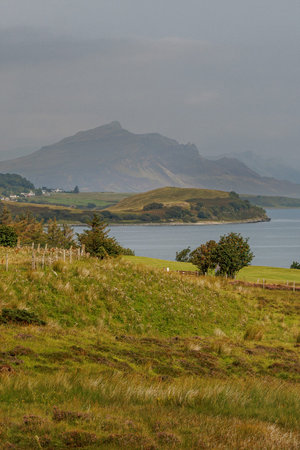 Scenic coastal landscape featuring lush grassy meadows and misty mountain peaks.