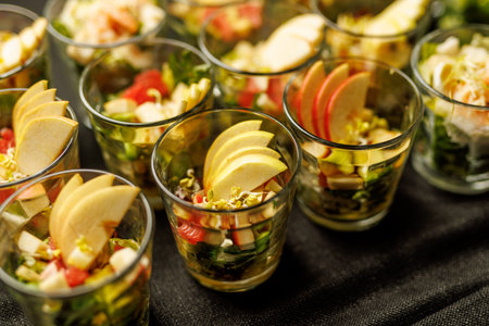 Rows of glass verrines filled with fresh salad and topped with thin apple slices on a dark...
