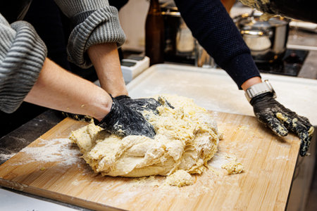 Two people are working together to prepare bread or pastry dough on a floured surface. They are...