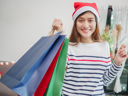 Asian beautiful smiling woman wearing Christmas hat with holding shopping bags and credit card, christmas shopping concept.の写真素材