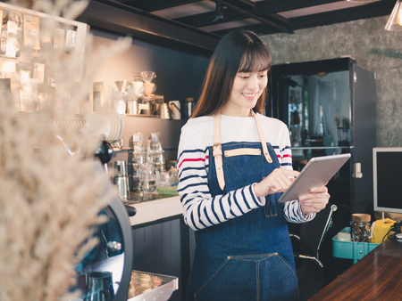 Young asian woman barista with a smile using tablet at bar counter, Owner small business concept.の写真素材