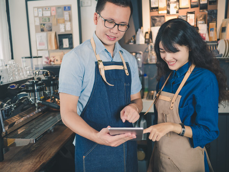 Young asian man and woman barista using taplet standing at bar counter, Owner small business concept.の写真素材
