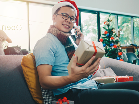 Asian man hand holding Christmas gift box. Using smartphone at cafe coffee shop.の写真素材