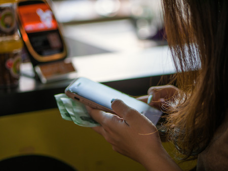 Close-Up of a young asian woman holding smartphone and touching screen payment at counter bar, Searching for social media in the city.の写真素材