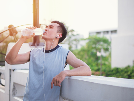 Handsome asian young man listening to music on earbuds and drink water, Healthy lifestyle concept.の写真素材