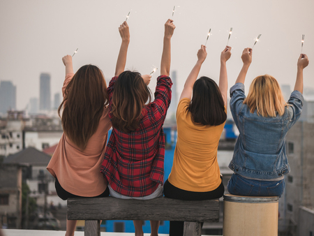 Young asian woman group of friends enjoying with fireworks, Young friends having drinks at rooftop in the city.の写真素材