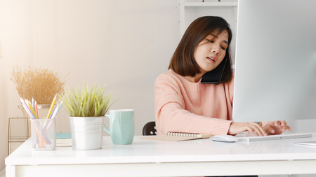 Young asian businesswoman using computer pc and smartphone at home office.の写真素材