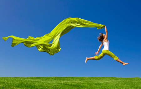 Beautiful young woman jumping on a green meadow with a colored tissue Beautiful young woman jumping on a green meadow with a colored tissue