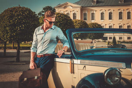 Confident wealthy young man with briefcase near classic convertible Confident wealthy young man with briefcase near classic convertible
