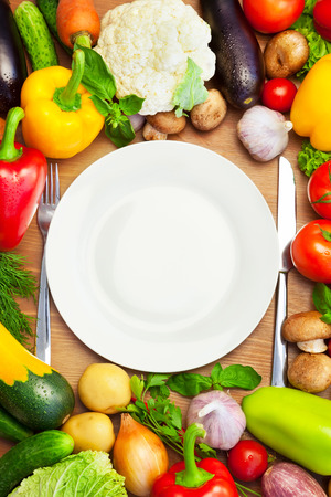 Fresh Organic Vegetables Around White Plate with Knife and Fork Vertical Composition Fresh Organic Vegetables Around White Plate with Knife and Fork Vertical Composition