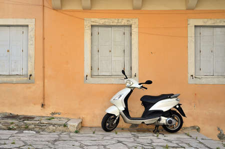 White scooter parking at the wall of the building. Scooter standing at the empty street of old Mediterranean townの写真素材