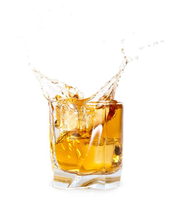 glass of whiskey with ice cubes splashing out over whiteの写真素材