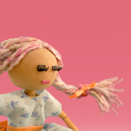 handmade wooden doll set against a solid pink background