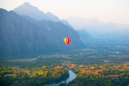 Striped hot air balloon flying over earth, evening landscape and the city with little houses, a river in Laos to Vang Vieng.の写真素材