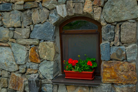 The monastery of stone, an old Church in the mountains. Alan Svyato-Uspensky monastery, which is located in Fiagdon.Hidixys.A window on stone wall background.Red flowers in a pot.の写真素材