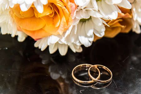 Two beautiful wedding rings and a wedding bouquet of orange roses and white colors.の写真素材