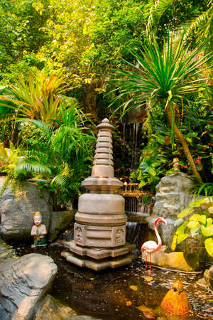 Small stupa on the background of green foliage and artificial waterfall. The statue Flamingo. Thailand. Bangkokの写真素材