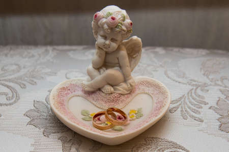 Two beautiful gold wedding rings lie on a platter in a rose shape with the angel sculptureの写真素材