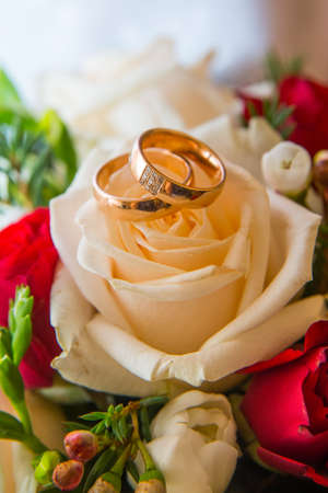 Two beautiful wedding gold rings with diamonds are on the bride's bouquet of red and white roses.の写真素材