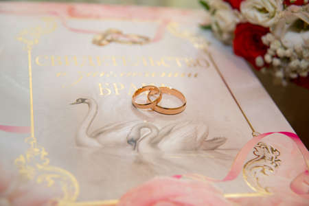 Two beautiful gold wedding rings lie on the background of the certificate of marriage with a pattern of swans and rings.の写真素材