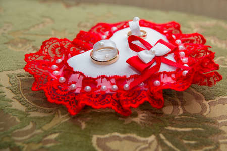 Two beautiful gold wedding rings lie on a cushion in the shape of a heart with a red laceの写真素材