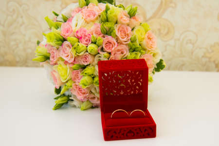 Gold wedding ring, a red box and a flower bouquet of the bride on the table