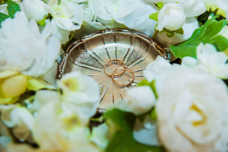 Two Beautiful wedding rings of the bride and groom lie on a plate near the flowers.の写真素材