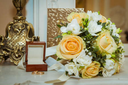 Beautiful bride bouquet with yellow roses, white flowers and gold rings with a crust on the wedding day.の写真素材