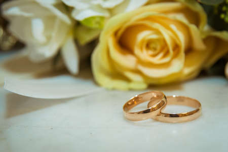 Two Beautiful gold rings of the bride and Groom lie near a bouquet of flowers. Yellow rose and white flowers.の写真素材