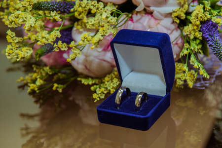 Two wedding rings are in a blue crust on the table. Bridal bouquet of beautiful pink peony flowers...