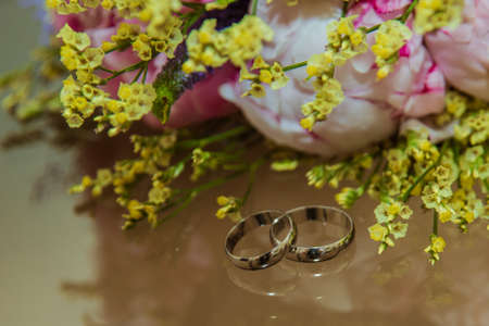 Two Beautiful gold rings of the bride and Groom lie near a bouquet of flowers. Pink peonies on your wedding day.の写真素材
