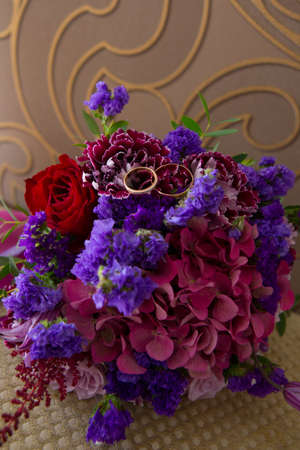 Two gold vintage wedding rings with diamonds bride and groom are on an unusual bouquet of lilac and violet flowersの写真素材