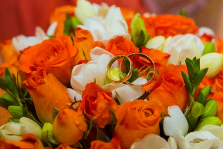 Wedding ring. Two gold vintage rings and a bride's bouquet of orange roses and white flowers.の写真素材
