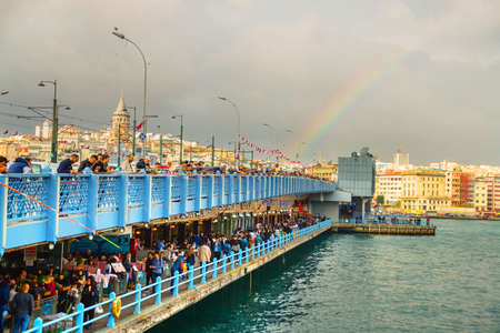 ISTANBUL, TURKEY - OCTOBER 2018: people fishing from the Galata bridge in cloudy weather. Downstairs restaurants with fresh fish. Galata tower and rainbow in the background.の写真素材