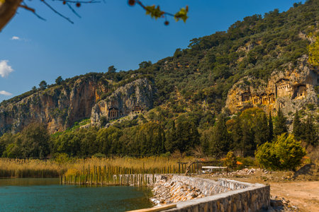 DALYAN, MUGLA, TURKEY: Rock-cut temple tombs of the ancient city Kaunos in Dalyan. Dalyan river view with ferry boats and carved tombs at background.のeditorial素材