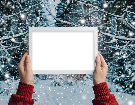 A person holds a blank white frame in front of a snowy winter scene, perfect for adding your own message or image.の素材